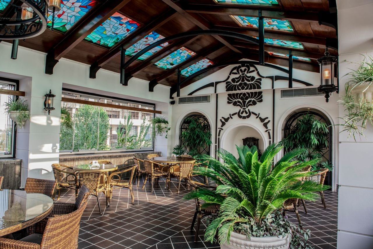 Inviting Persian cafe interior featuring stained glass, wicker furniture, and lush greenery.